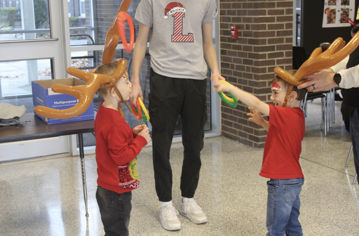 Senior Jacob Elliot having fun with two little boys dressed up as reindeer trying to hook rings on each others antlers